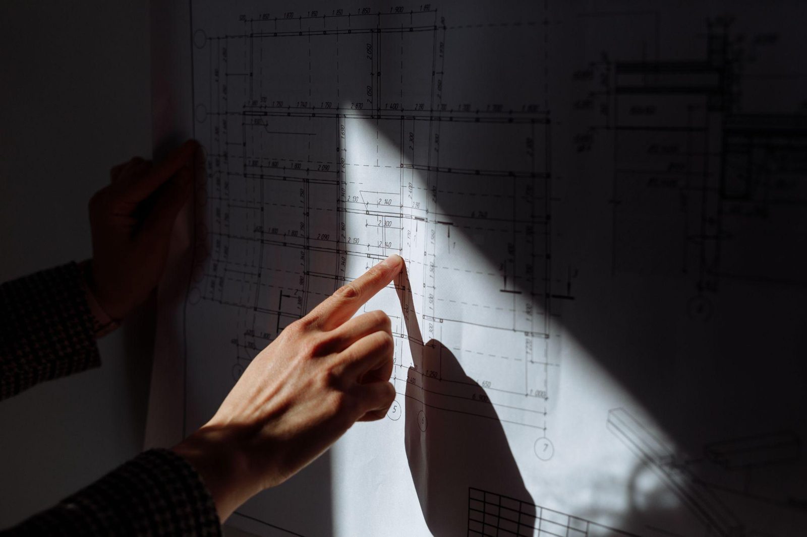 Hand pointing to an architectural floor plan under a beam of light