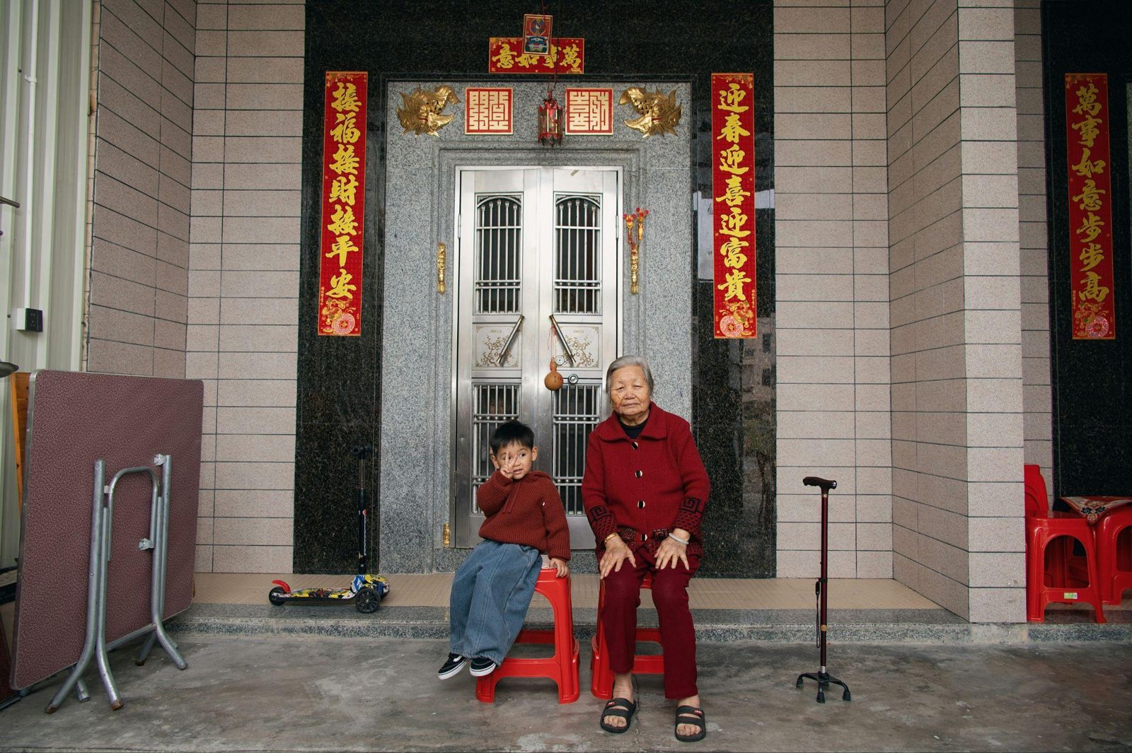 Elderly woman and young boy sitting outdoors in front of a traditional doorway