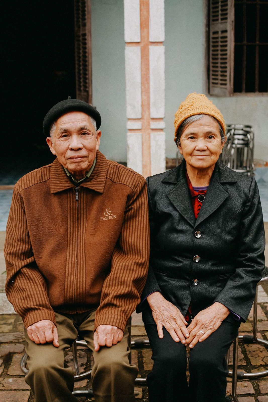 Elderly East Asian couple sitting side by side outdoors, looking calmly toward the camera